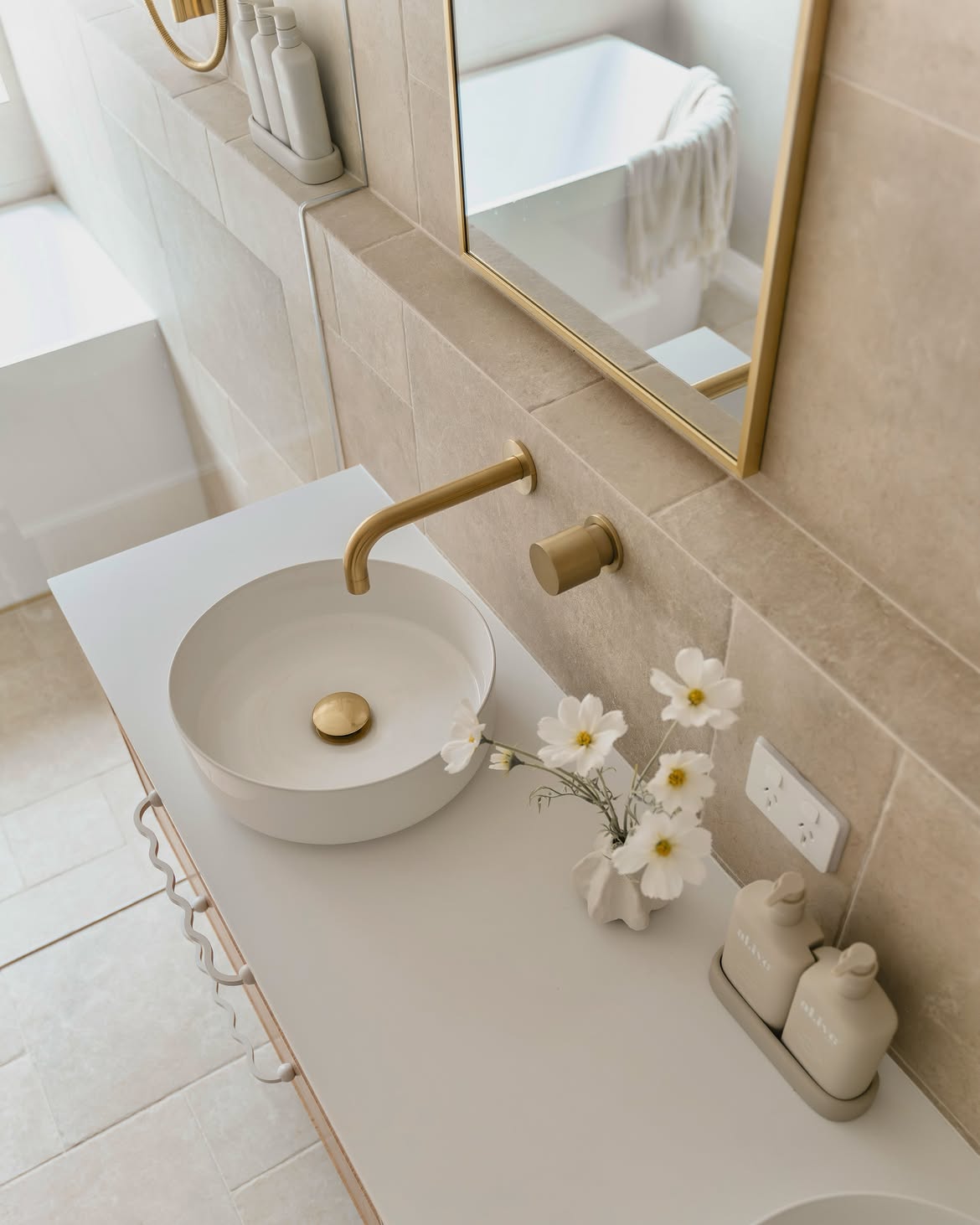 Soft beige bathroom with gold tapware, framed mirror and white basin