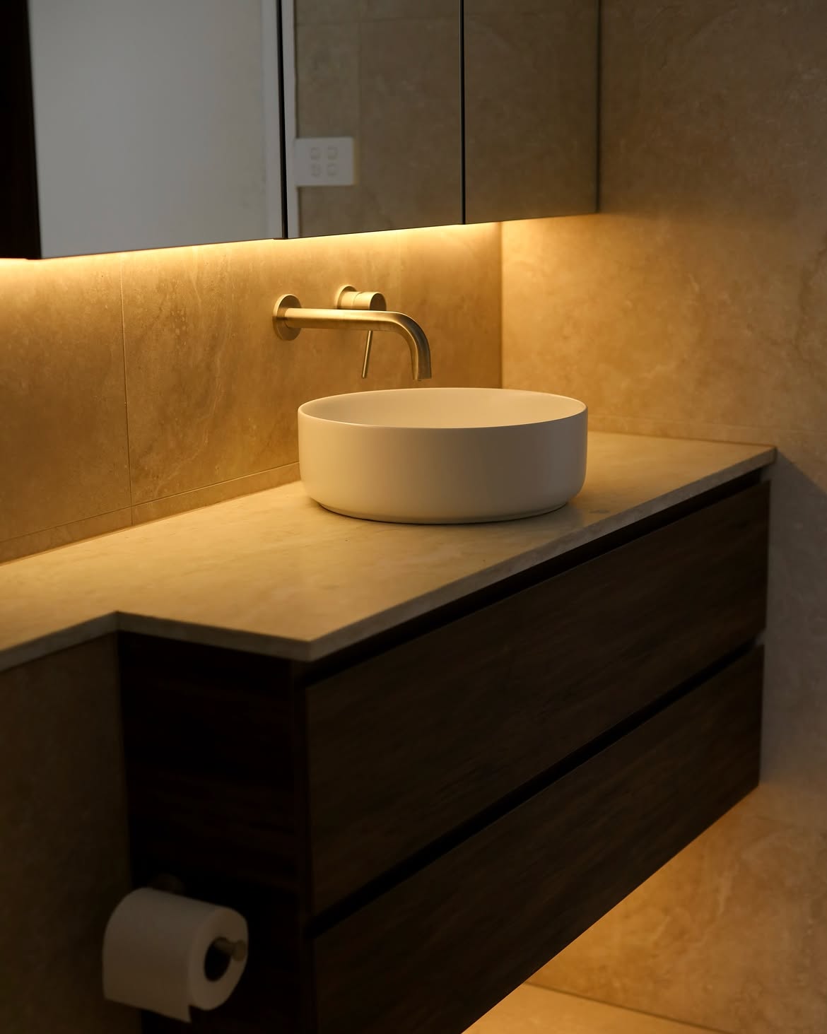 Warmly lit vanity with white basin and gold tapware
