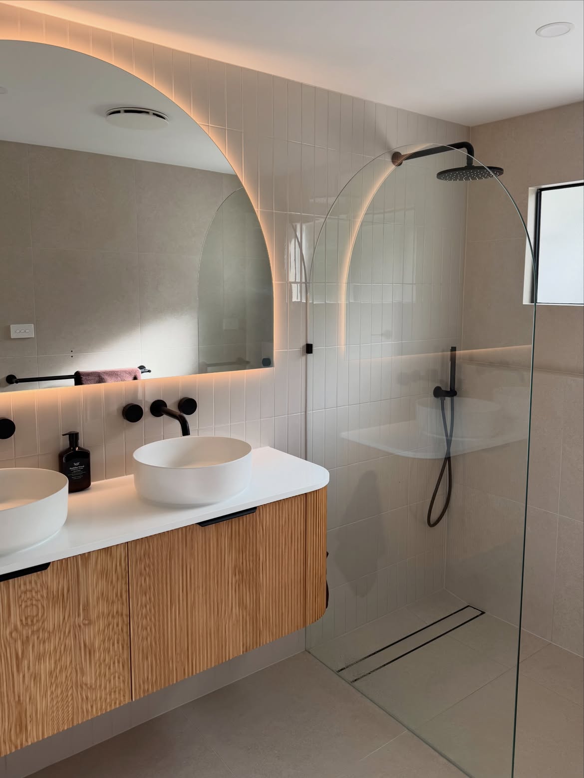 Curved timber vanity, white basins, arch mirror and black shower fittings